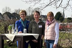 Drei Frauen stehen hinter einem Stehtisch und schauen freundlich in die Kamera. Klick führt zu Großansicht.
