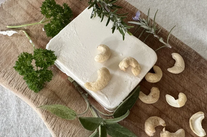 Veganer Feta auf einem Holzbrett mit Cashewnüssen. Klick führt zu Großansicht.