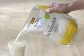 Ein Beutel in dem Milch ist. Aus diesem wird gerade Milch in ein Glas geschüttet.