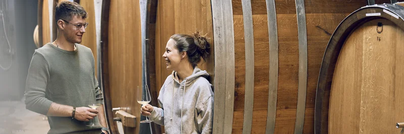 Ein Mann und eine Frau in einem Keller voller Holzfässer für Wein.
