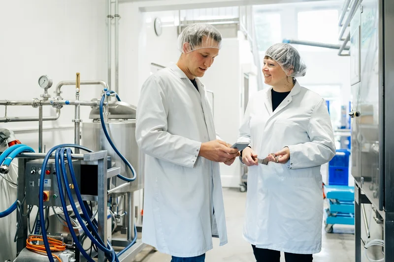 Eine Frau und ein Mann in Laborkitteln bei einer Besprechung in einem Labor. Klick führt zu Großansicht.