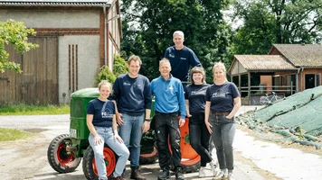 Sechs Menschen stehen vor oder auf einem Traktor und lachen freundlich in die Kamera.