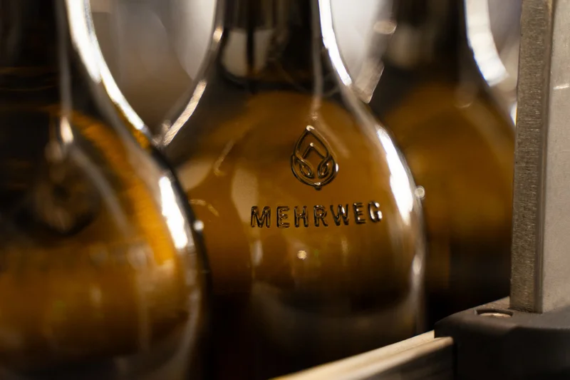 Nahaufnahme der Weinmehrwegflasche. Zu sehen ist das Wort "Mehrweg", geprägt im Glas der Flasche. Klick führt zu Großansicht.
