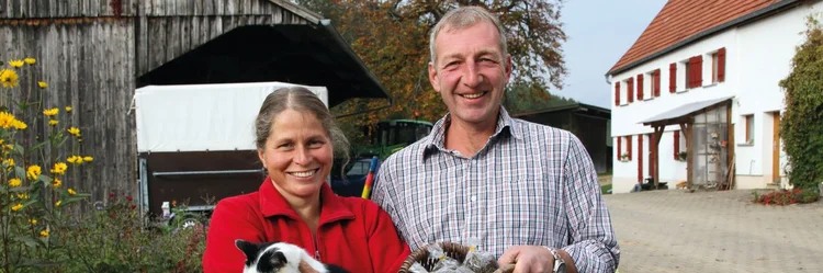 Eine Frau mit einer Katze auf dem Arm und ein Mann mit einem Korb Linsen