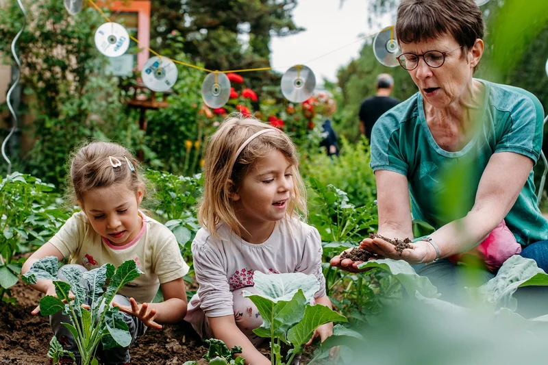 Erzieherin mit Kindern im Gemüsebeet. Klick führt zu Großansicht in neuem Fenster.