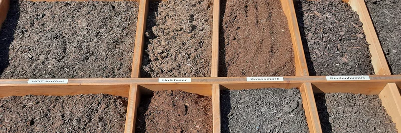 Verschiedene Torfersatzstoffe zur Ansicht in Holzkästen.