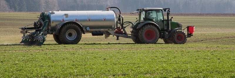 Ein Traktor zieht ein Güllefass über eine landwirtschaftliche Fläche. 
