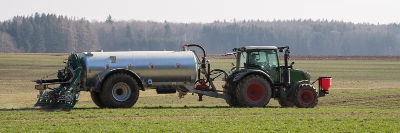 Ein Traktor zieht ein Güllefass über eine landwirtschaftliche Fläche.