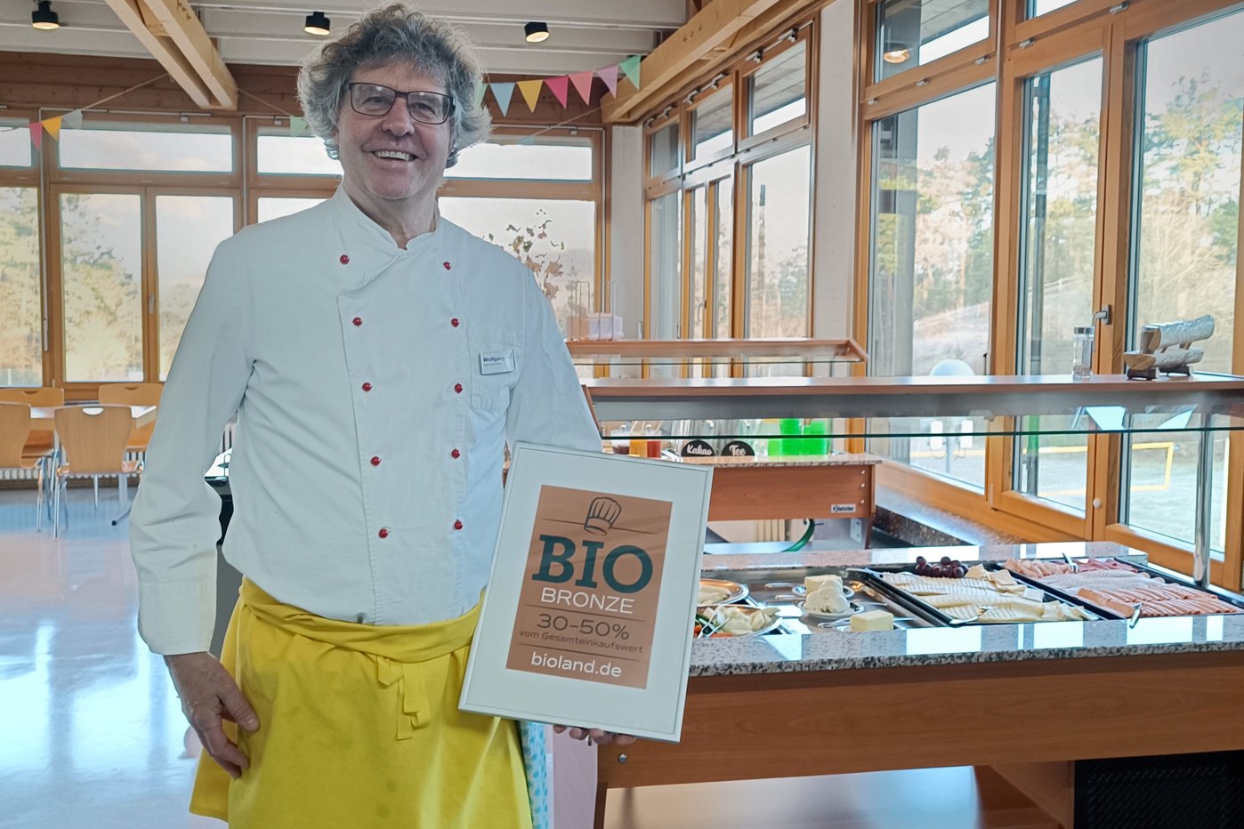 Küchenleiter Wolfgang Kress zeigt stolz das Bioland-Zertifikat Bronze. Klick führt zu Großansicht in neuem Fenster.