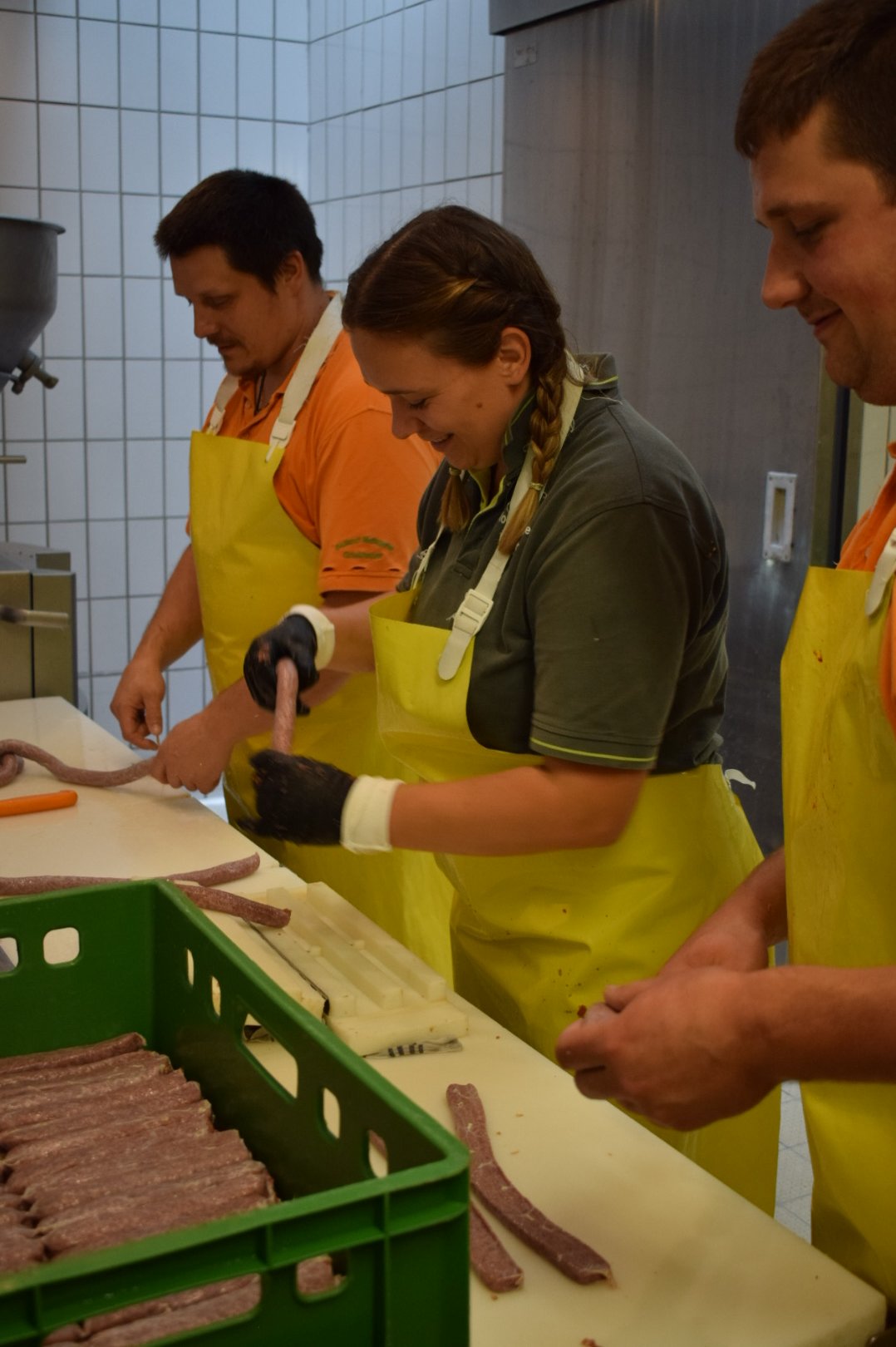 Eine Frau und zwei Männer beim Wurst machen. Klick führt zu Großansicht.