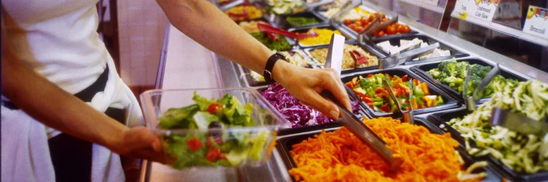 Frau bereitet sich Salat an einer Salatbar zu. 