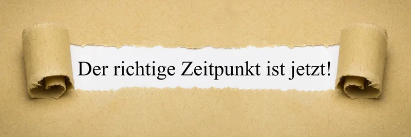 Ein sandfarbener Untergrund auf dem eine weiße Fläche freigeschaufelt ist. In dieser weißen Fläche steht "Der richtige Zeitpunkt ist jetzt!"