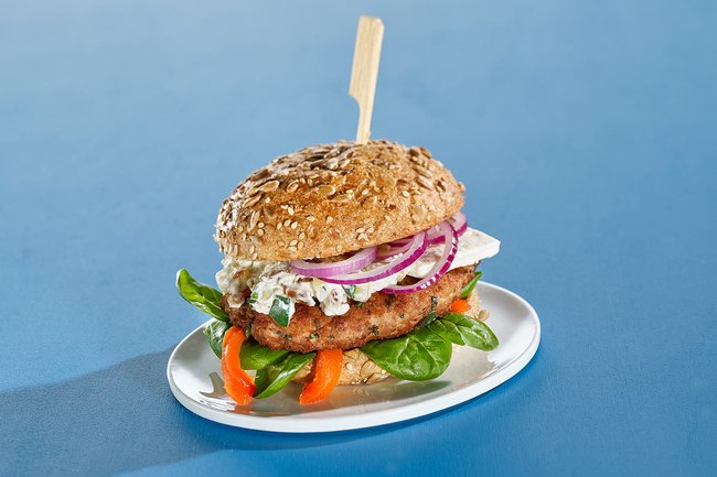 Lamm-Burger mit weißen Bohnen, Feta-Schafskäse, eingelegter Paprika und Zucchini-Dip auf einem Teller angerichtet.
