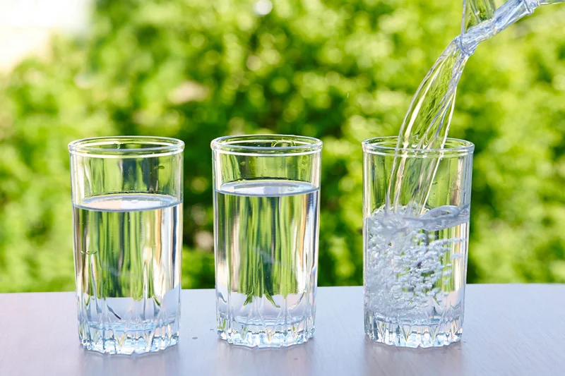 Drei volle Wassergläser stehen nebeneinander, eins wird befüllt