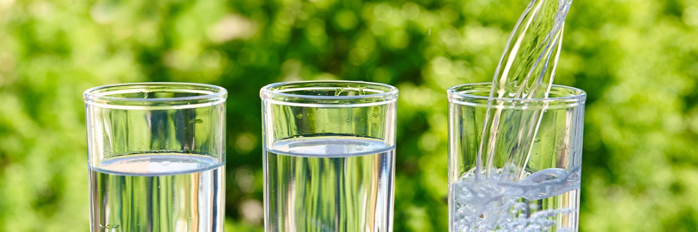 drei Wassergläser nebeneinander vor grünem Hintergrund.