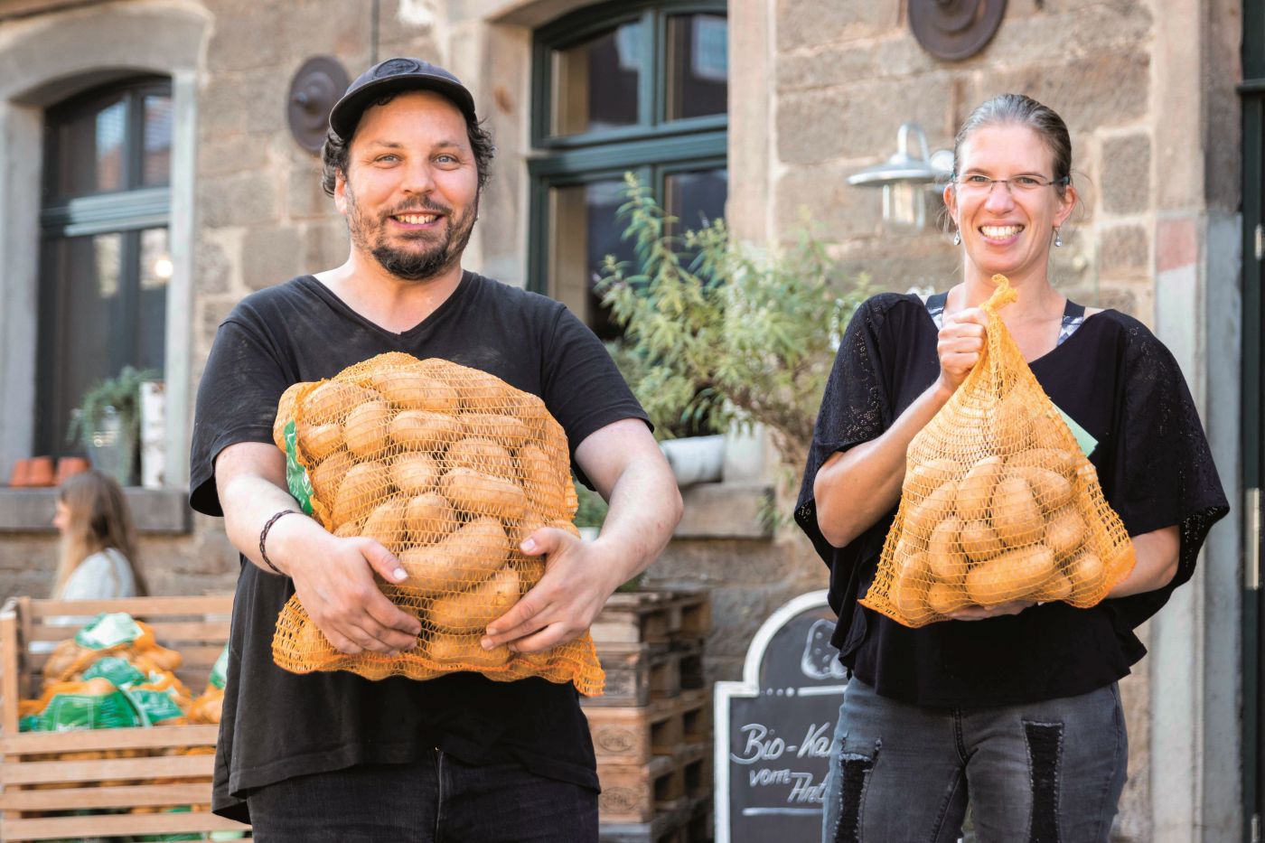 Mann und Frau halten jeweils einen Sack Kartoffeln in den Armen.