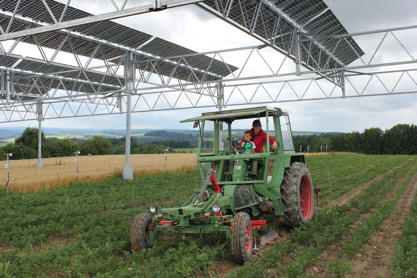 Traktor mit Landwirt und Kind auf einem Kartoffelacker mit Solaranlage. Klick führt zu Großansicht im neuen Fenster.
