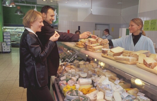 Verkäuferin bietet Kunden Käse zum Probieren an. Klick führt zu Großansicht im neuen Fenster.