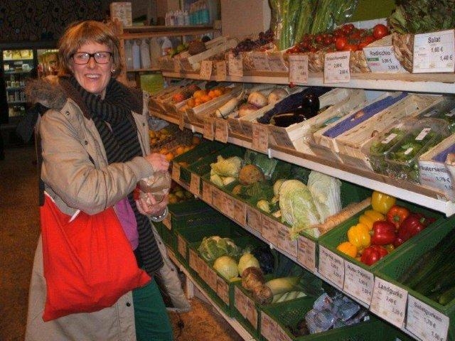 Eine Frau packt Gemüse aus einem Gemüseregal in eine Papiertüte.